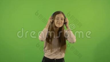 一个漂亮的年轻白人模特通过耳机和舞蹈听音乐。 在绿色的背景上。